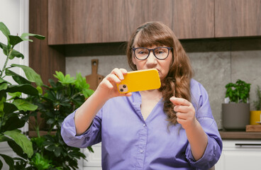 Elderly woman in glasses chatting on smartphone, placing online order or reading social networks...
