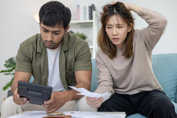 Stressed and headache asian couple with large bills or invoices no money to pay to expenses and...