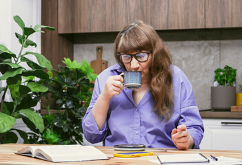 Old woman drinking coffee while busy studying with books and notebooks in stylish modern apartment