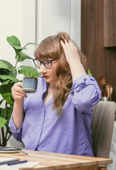 Elderly woman drinking coffee from blue cup while working at desk in stylish modern apartment
