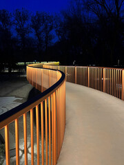 Curved pathway with illuminated wooden railings at dusk