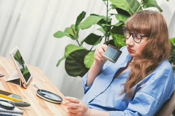 Elderly business woman drinking coffee from blue cup while working at desk in stylish modern...