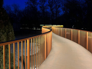 Illuminated walkway with golden railings curving through a park at dusk