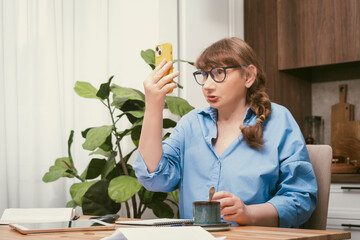 Serious elderly woman talking on smartphone and makes notes in notebook in stylish modern flat