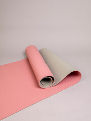 Double-sided pink and gray sports yoga mat in a half-open roll lies on a gray background