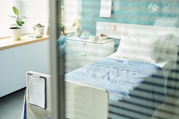 Hospital room showing empty patient bed with blue blanket, bedside table with medical items,...