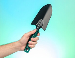 Hand holding a garden trowel with a green handle against a gradient background.
