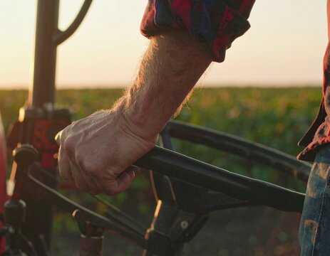 Close-up of a farmer's arm and hand gripping a tractor's steering wheel, driving.