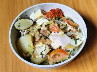 A bowl of Indonesian chicken soto with shredded chicken, sliced boiled egg, vermicelli, sliced cabbage, bean sprouts, celery, chili sauce and lime, mixed with delicious sauce. On a wooden table.	
