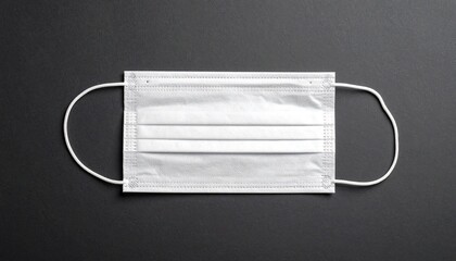 White disposable face mask with pleats and elastic ear loops placed on a dark surface