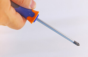 The hand is holding a screwdriver with an insulated handle. Close-up. Soft focus. 