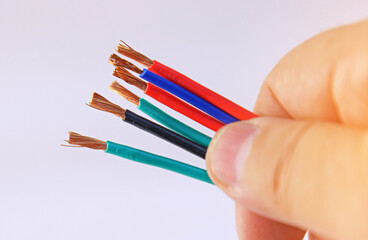 The hand is holding a copper electrical insulated mounting wire. Close-up. Soft focus. 