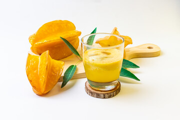 Star fruit juice with fresh star fruit and green leaves on a light background displays freshness.