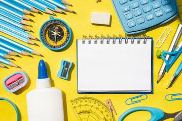 Vertical flat lay with school supplies including spiral notebook, glue, pencils, and markers on yellow background. Back to school creative template.