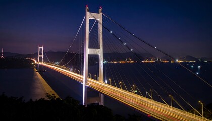 Fototapeta premium Illuminated suspension bridge spanning a body of water at night.