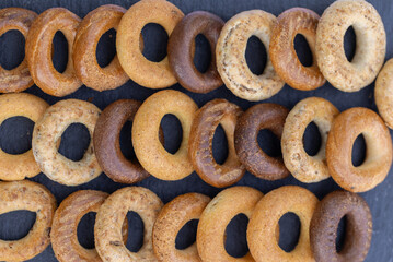 Freshly baked mini bagels on a dark background. Top view. Pretzels in the form of a ring close-up. Small bread circle biscuit. Bowls with different types of bagels.
