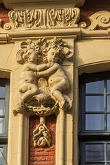 architectural relief features two cherubic figures holding grape clusters, seated symmetrically above a decorative window frame of historic buildings in Lille, France.