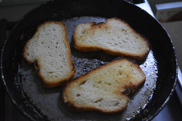 Food, food products, white sliced bread, loaf. Pieces of white bread with a toasted crust lie on a hot old metal frying pan.