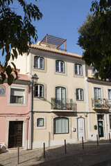 Obraz premium Traditional Portuguese house with balcony and green doors in Carnide, Lisbon, Portugal. The facade features potted plants, flags, and cobblestone street in front, under clear blue sky.