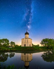 Obraz premium Night scene of a white church reflected in calm water under a starlit sky showing the Milky Way