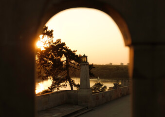 Sunset view of the Danube River and a lantern tower framed by an arch in Kalemegdan Fortress,...