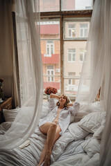 sexy woman in white shirt in bed by the window