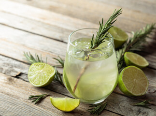 Hard seltzer with ice, rosemary, and lime slices on an old wooden table.