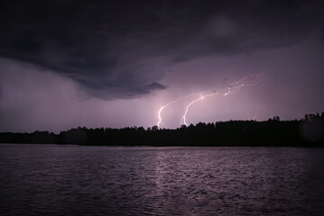 Lightning storm over a dark lake with forest silhouette under dramatic night clouds.