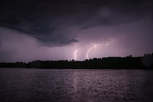 Lightning storm over a dark lake with forest silhouette under dramatic night clouds.