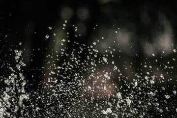 suspended water droplets in motion against a dark background, creating a sparkling abstract pattern with light reflections.