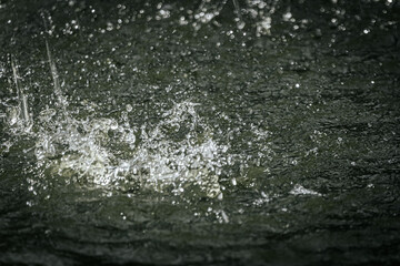raindrops splashing on water, capturing droplets and ripples in motion with a dramatic, dark background.
