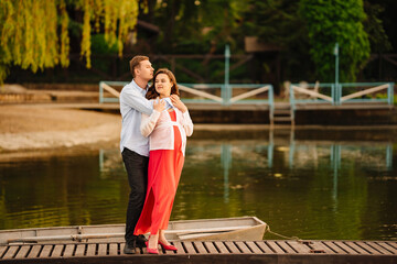 man and pregnant woman in red dress at sunset on the pier 