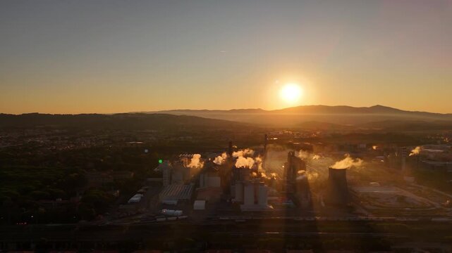 Drone aerial of large industrial factory with massive smokestacks across vast area at sunset, dramatic industrial landscape with glowing evening sky