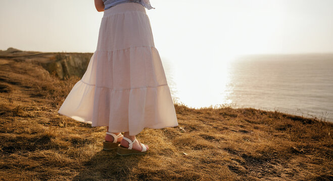 Flowing summer skirt and sandals at golden sunset on seaside cliff
