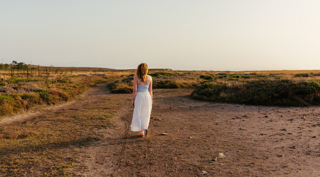 Back view of woman walking along dirt path at sunset