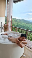 Handsome Man Unwinding in Bubble Bath with Stunning Mountain View at Twilight