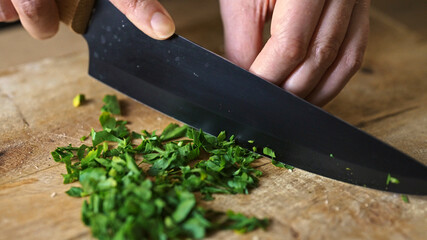 Chopping fresh parsley on wooden cutting board.