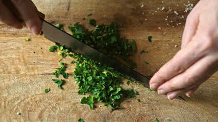 Chopping fresh parsley on wooden cutting board.