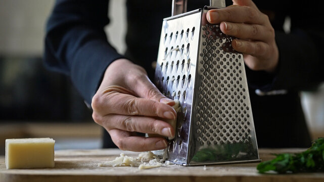 Grating hard cheese on metal kitchen grater.