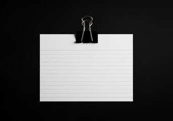 Blank white card held by black binder clip on black background