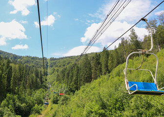 A summer mountain landscape where a chairlift moves over a dense forest, revealing a picturesque...