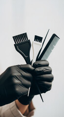 Hand in black glove holding hair coloring brushes and comb