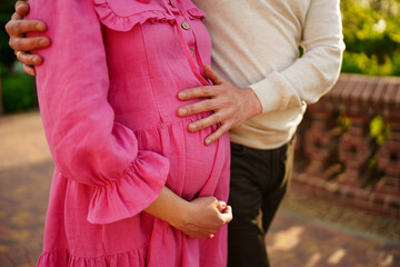 A man holds on to the tummy of a pregnant woman with his hands. 