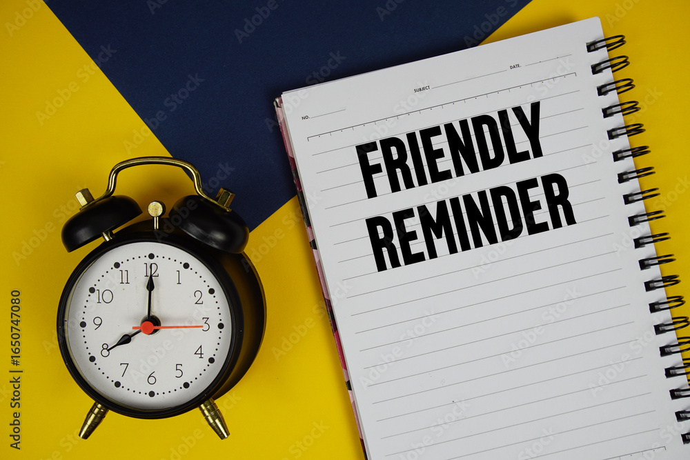 Poster friendly reminder text written on notepad with alarm clock on yellow background