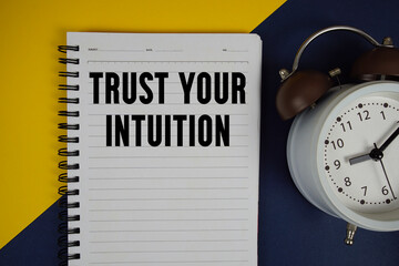 Trust Your Intuition text written on notepad with alarm clock on yellow background