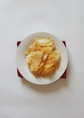 Plate of crispy potato chips with black pepper on white surface