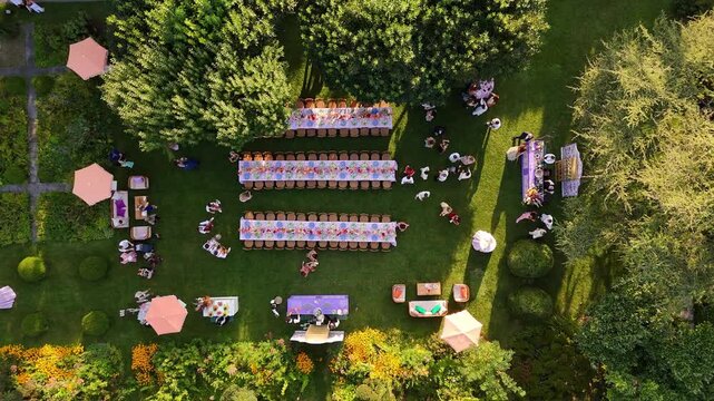 Drone top view of luxury wedding party at Lake Como villa, Italy. Guests at long tables with stylish colorful decor on green lawn for daytime destination celebration