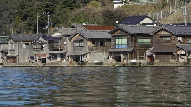 A row of traditional Funaya boathouses lines the waterfront of the fishing village of Ine on a clear winter day. Ine, Kyoto, Japan.