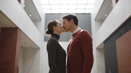 kiss and romance - A couple sharing a romantic kiss in a modern architectural space with large windows, soft lighting, and minimalist design, creating an intimate atmosphere