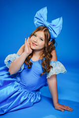 Cute teenage girl in blue doll dress with big blue bow posing lying on the floor